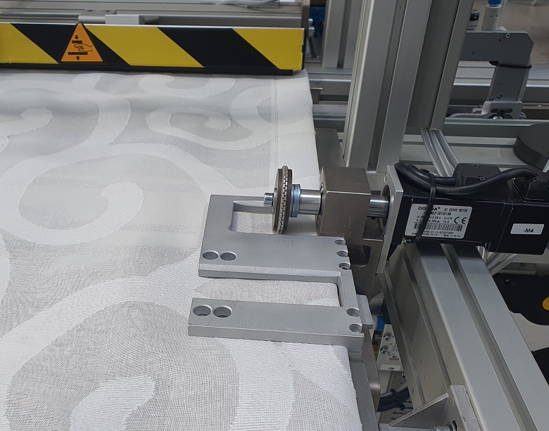 Vista en primer plano del mecanismo de sellado por ultrasonidos, mostrando la rueda que confecciona el dobladillo de la cortina técnica de forma automática y sin necesidad de hilo.