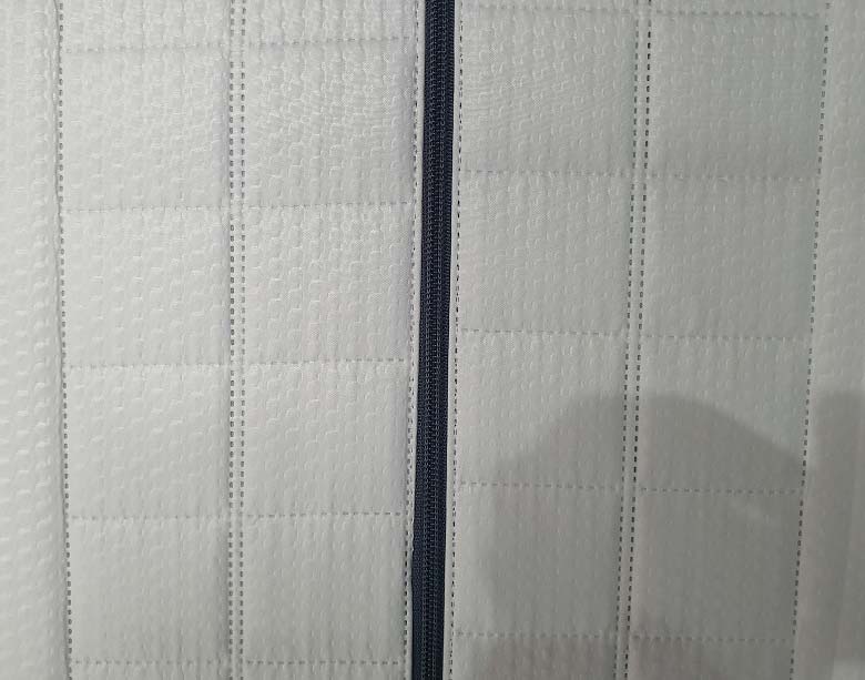 Primer plano de la platabanda de colchón terminada, mostrando la costura múltiple de diseño, la cremallera insertada y el borde sellado limpiamente gracias al corte por ultrasonidos.