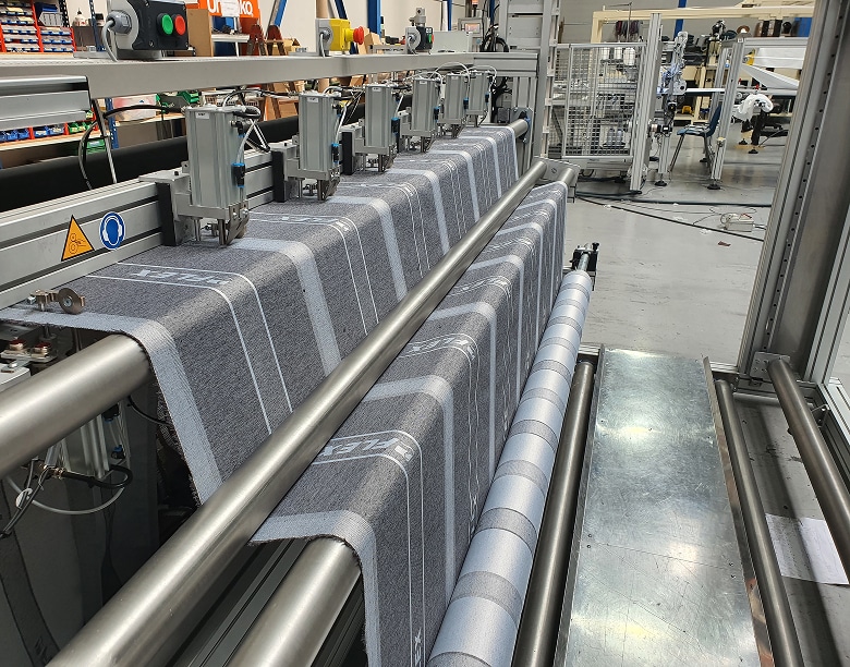 Vista de la zona de inspección de la máquina, mostrando el pasillo de acceso seguro donde el operario puede realizar el control de calidad del tejido acolchado en tiempo real.